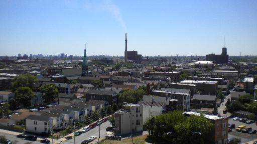 Wide angle view of a cityscape with various buildings and a factory in the background.