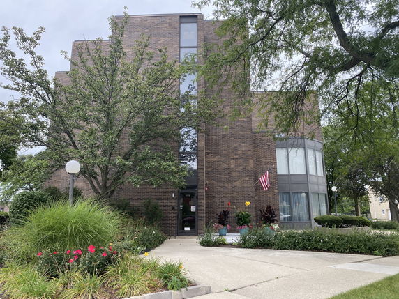 Front view of a multi-story brick building with large windows and surrounding greenery.