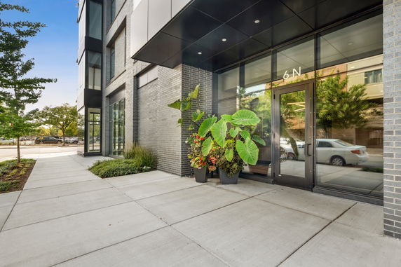 Front view of a modern building entrance with large glass doors and potted plants.