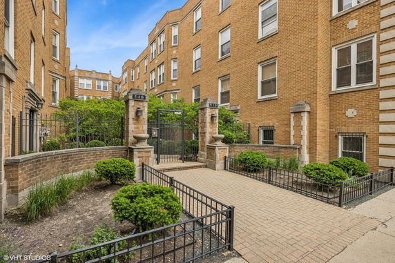 Front view of a multi-story brick apartment building with a gated entry.