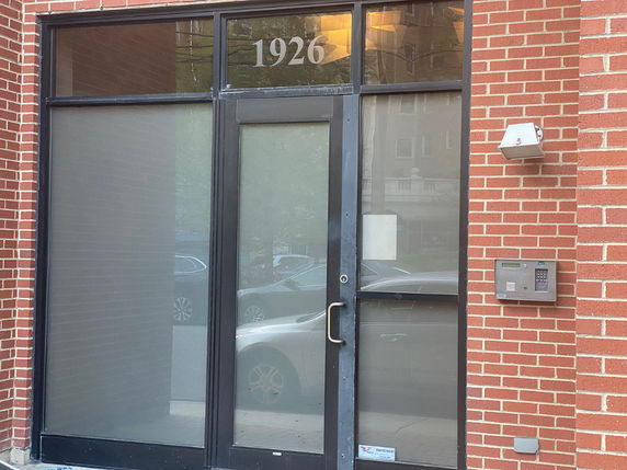 Entrance of a brick building with a glass door and keypad entry system.
