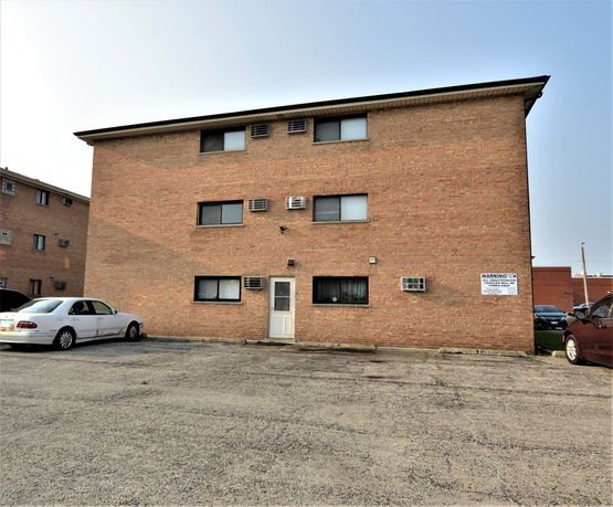Front view of a three-story brick building with parking area.
