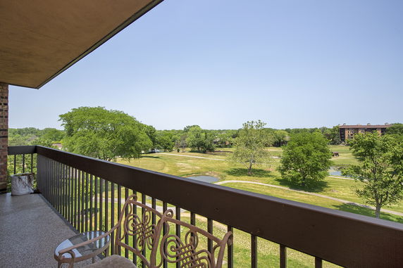 Wide angle view from a balcony overlooking a green landscape with trees and distant buildings.