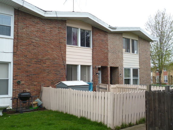 Front view of a two-story brick townhouse with a small fenced yard.