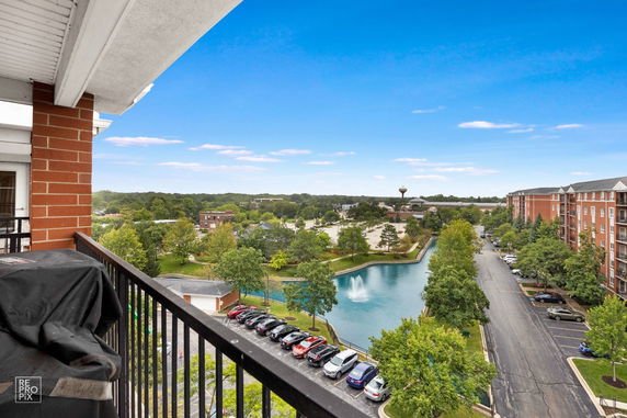 Panoramic view from a balcony overlooking a water feature, parking area, and surrounding greenery.
