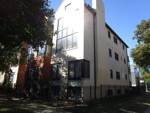 Front view of a multi-story residential building with large windows and a fenced walkway.
