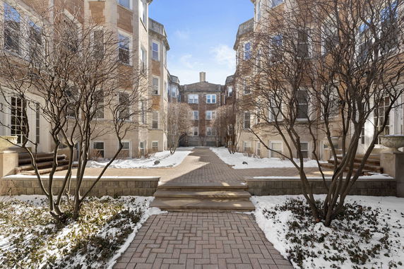Front view of a multi-story residential building with snow-covered pathways and bare trees.
