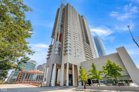 Front view of a tall modern building with multiple balconies and a glass facade.