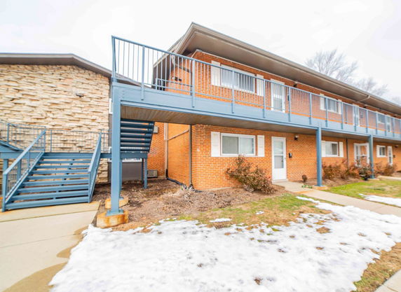 Front view of a two-story brick apartment building with a blue staircase and balcony.