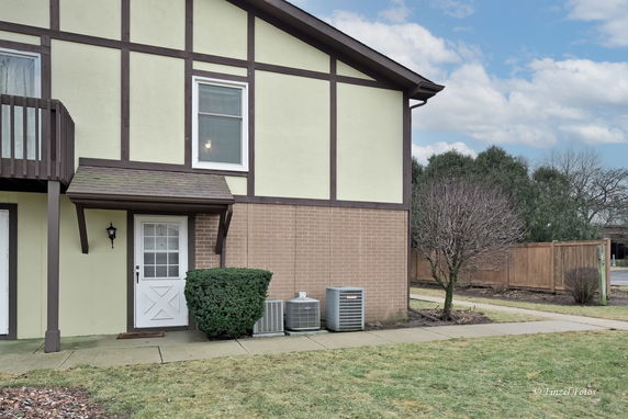 Front view of a house with a beige and brown exterior and air conditioning units.