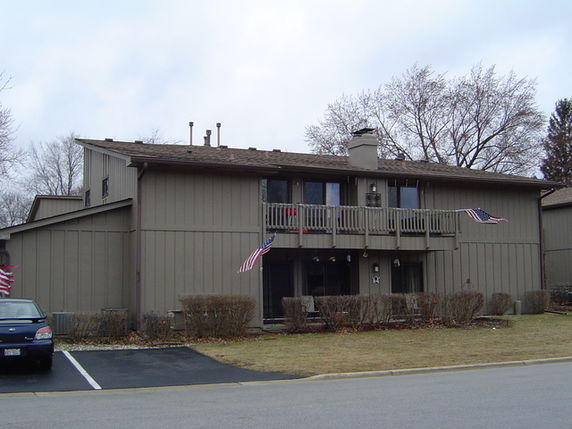 Front view of a two-story house with balconies and American flags.