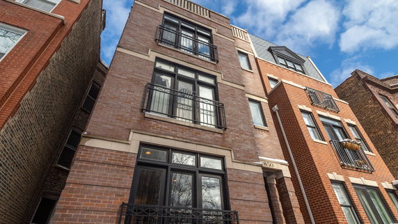 Front view of a multi-story brick building with black metal railings and large windows.