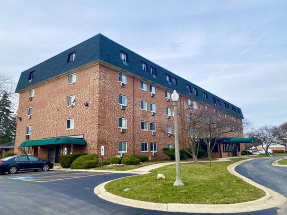 Front view of a four-story brick building with green awnings and a dark roof.