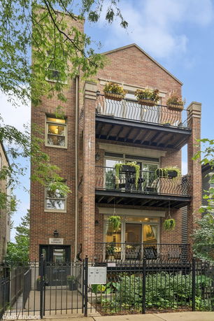 Front view of a three-story brick building with balconies and a gated entrance.
