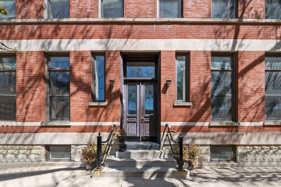 Front view of a brick building entrance with steps leading to a dark wooden door.