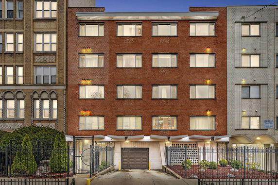 Front view of a multi-story brick apartment building with numerous windows and a gated entrance.