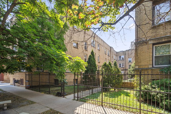 Front view of a multi-story brick apartment building with a gated entrance.