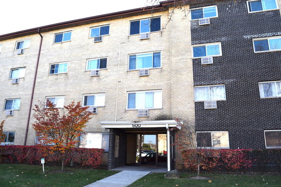 Front view of a multi-story apartment building with beige and dark brown brick exterior.