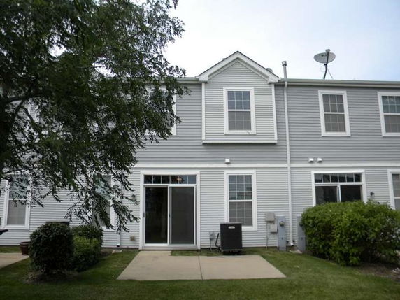 Back view of a two-story townhouse with a sliding glass door and several windows.