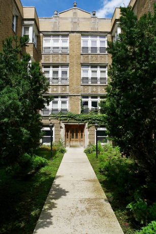 Front view of a multi-story apartment building with brick exterior and greenery.