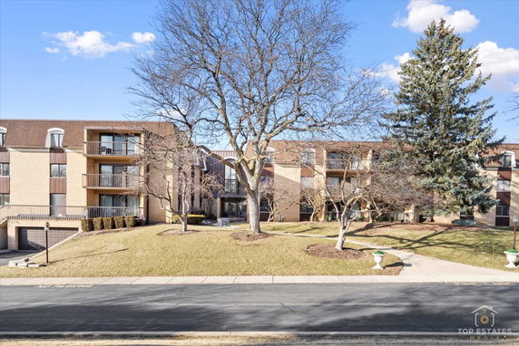 Front view of a multi-story apartment building with balconies and a sloped roof.