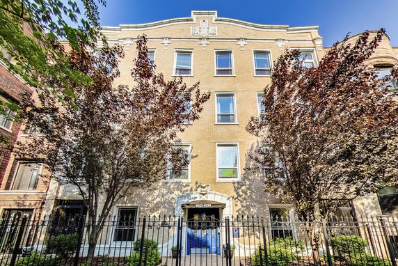 Front view of a multi-story brick building with several windows and a gated entrance.