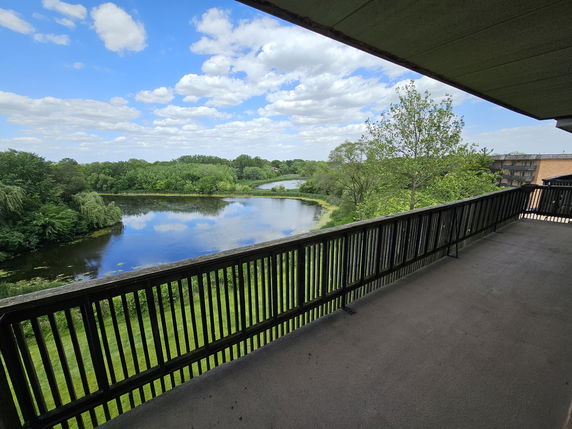 Panoramic view from a balcony overlooking a lake and green landscape.