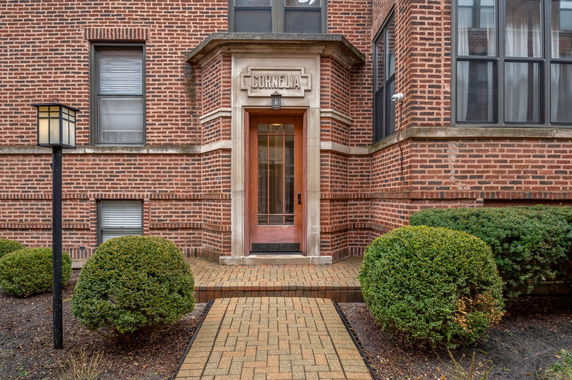 Front entrance of a brick building with a decorative doorway and small bushes.
