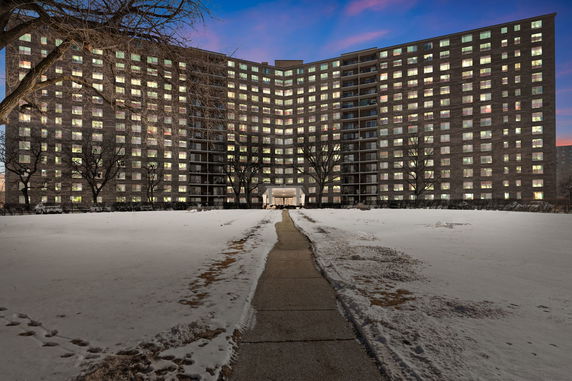 Front view of a multi-story building with numerous lit windows and a path leading to the entrance.