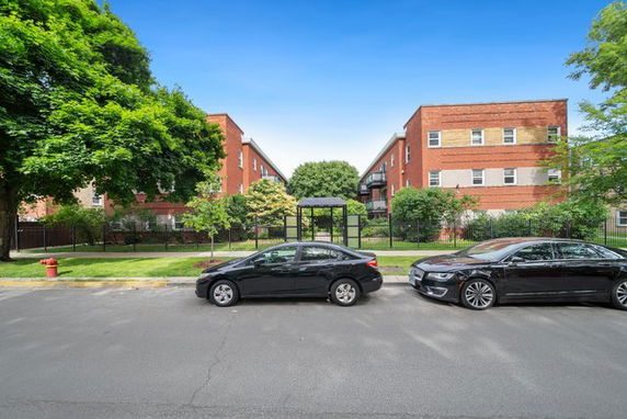 Front view of two three-story brick apartment buildings with a central walkway and parking area in front.