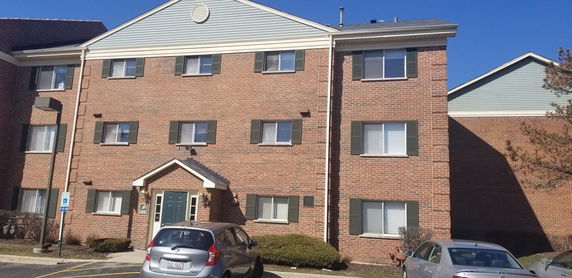 Front view of a three-story brick apartment building with green shutters and multiple windows.