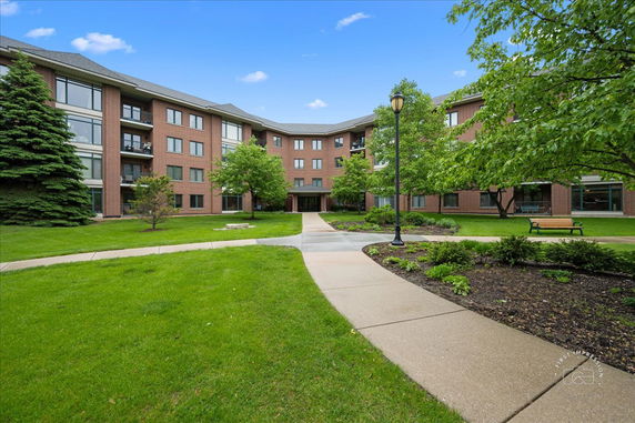 Front view of a four-story brick building with balconies and windows, surrounded by trees and a paved walkway.
