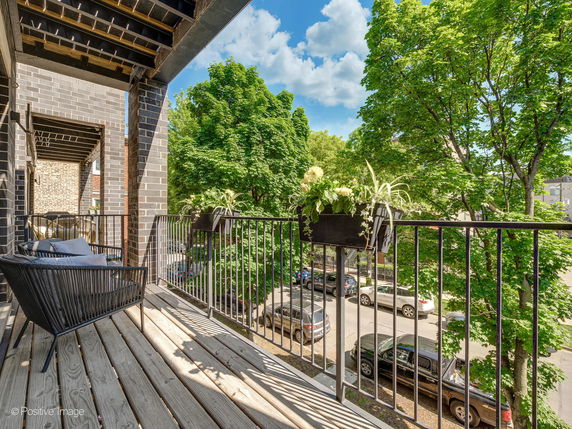 Balcony view with railing, plants, and neighborhood street with trees.