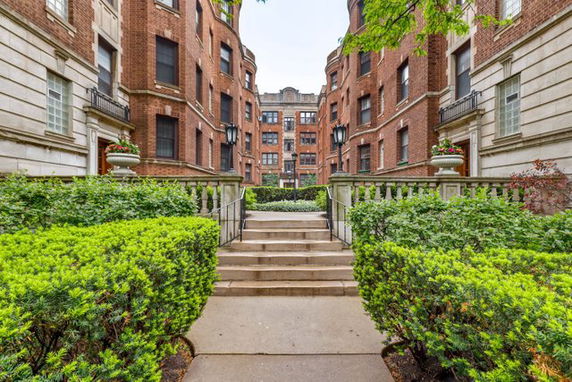 Front view of a multi-story brick building with ornate railings and landscaped entrance.