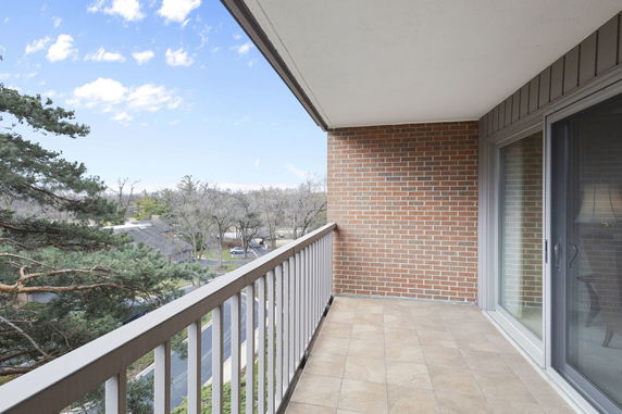 View from a balcony with a brick wall and sliding glass doors, overlooking trees and a road.