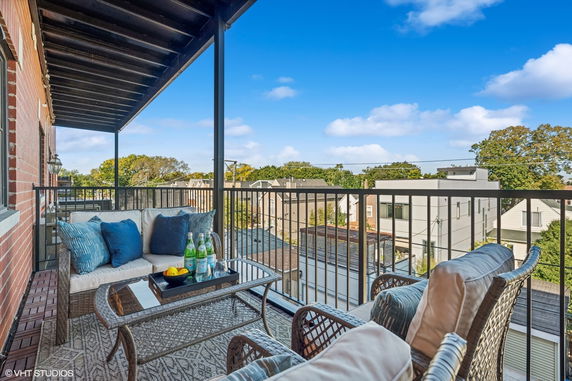 Outdoor balcony with a seating area and view of surrounding neighborhood.