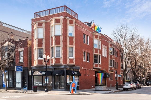 Front view of a multi-story brick building with bay windows and a rooftop deck.
