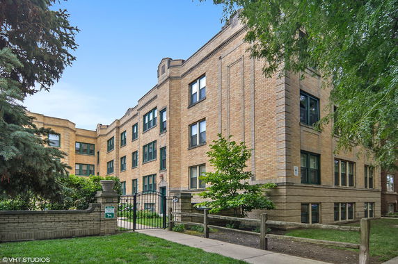 Front view of a multi-story brick apartment building with a gated entrance.