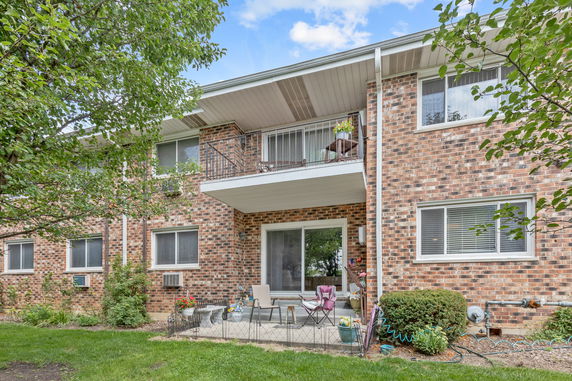 Rear view of a two-story brick residential building with balconies and a small patio area.