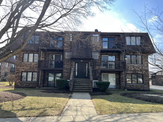 Front view of a three-story brick apartment building with balconies.