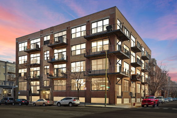 Front view of a multi-story brick building with balconies at sunset.