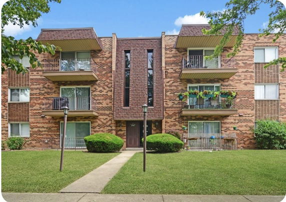 Front view of a three-story brick apartment building with balconies.