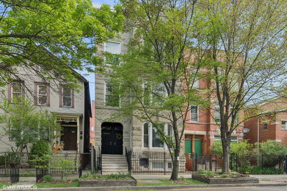 Front view of a three-story residential building with a stone facade and arched entrance.