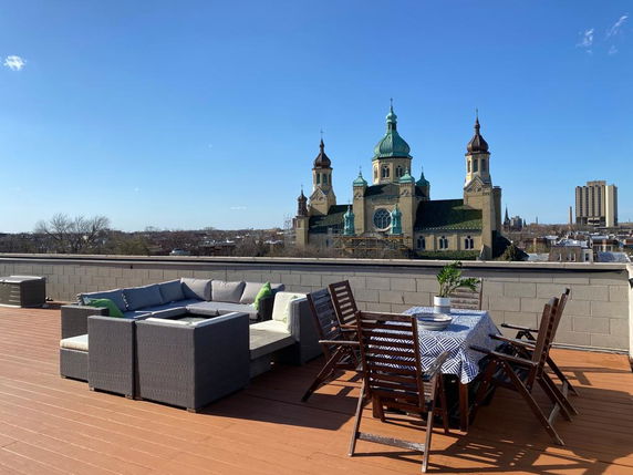 Rooftop with seating area and dining table overlooking a historic building with towers.