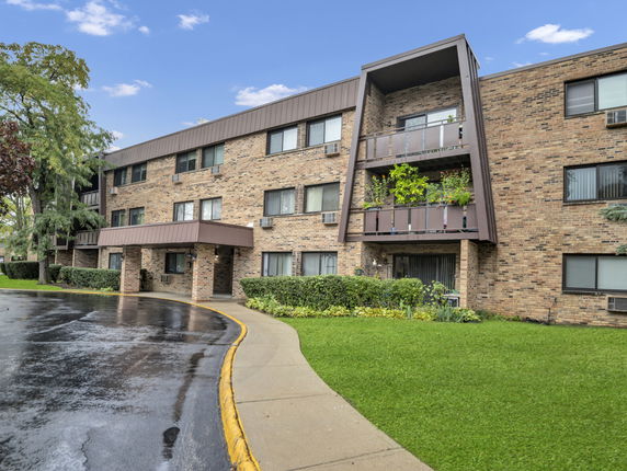 Front view of a three-story brick apartment building with balconies.