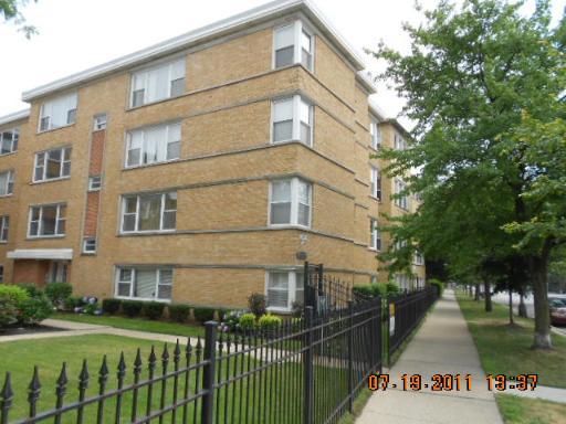 Front view of a multi-story brick apartment building with a fence and sidewalk.