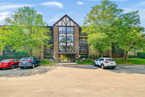 Front view of a brick apartment building with large windows and parking area.