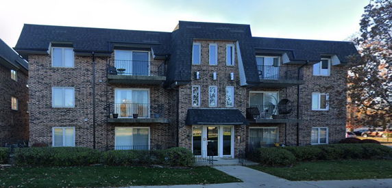 Front view of a multi-story brick apartment building with balconies and large windows.