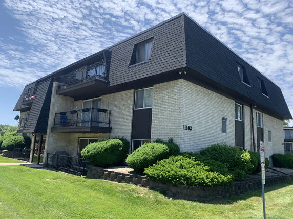 Front view of a multi-story apartment building with balconies and a dark shingle roof.