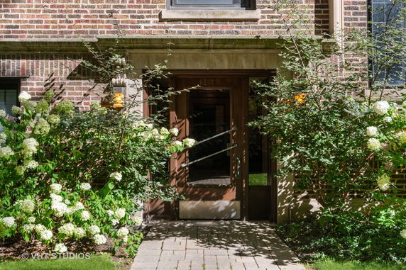Front view of a brick building entrance with plants and flowers surrounding the doorway.